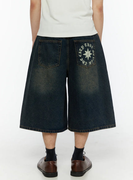 Men's 'Never Stop' Graphic Bermuda Jorts (Dark Blue) IL507 back view on model showing wide-leg fit star compass graphic pocket and acid-wash denim texture