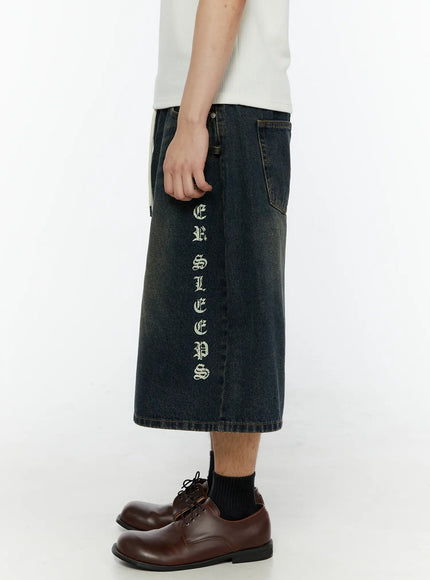 Men's 'Never Stop' Graphic Bermuda Jorts (Dark Blue) IL507 side view on model showing full leg length vertical graphic print and wide-leg washed denim silhouette