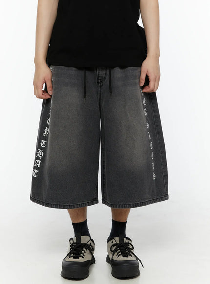 Men's 'Never Stop' Graphic Bermuda Jorts (Dark Gray) IL507 front close-up on model showing wide-leg silhouette drawstring waist and vertical letter graphics on both legs