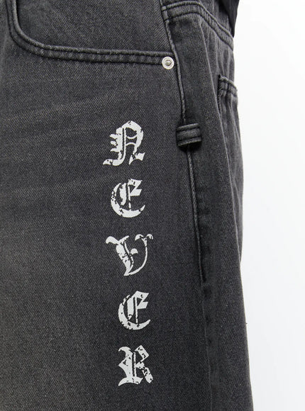 Men's 'Never Stop' Graphic Bermuda Jorts (Dark Gray) IL507 detail close-up of front right hip showing vertical old English gothic letter print on washed dark gray denim with coin pocket