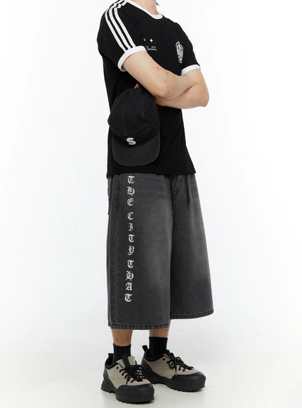 LEWKIN Men's 'Never Stop' Graphic Bermuda Jorts (Dark Gray) IL507 side view on model arms crossed showing vertical old English letter graphic on leg