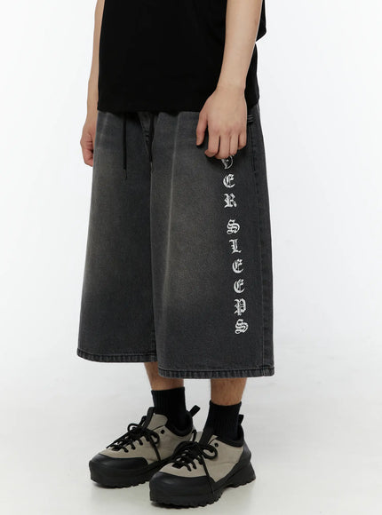 Men's 'Never Stop' Graphic Bermuda Jorts (Dark Gray) IL507 side close-up on model showing right leg vertical old English letter graphic and drawstring elastic waistband