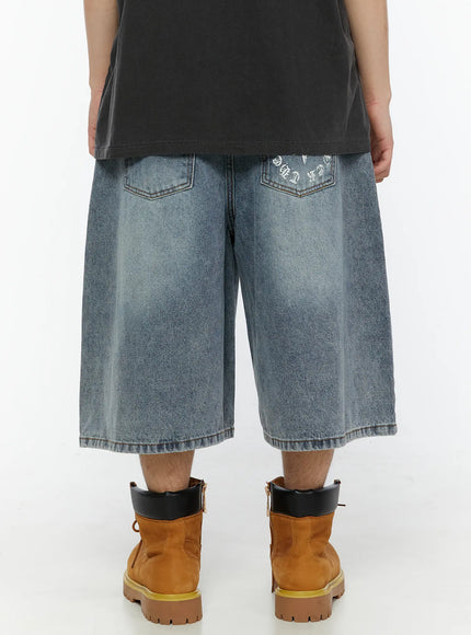 Men's 'Never Stop' Graphic Bermuda Jorts (Light Blue) IL507 back view on model, two back pockets with old-english star graphic print on right pocket, wide-leg washed denim, styled with tan boots