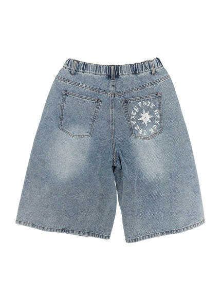 Men's 'Never Stop' Graphic Bermuda Jorts (Light Blue) IL507 flat-lay back view, light blue washed denim, right back pocket with old-english circular text and eight-point star graphic, elastic waistband detail