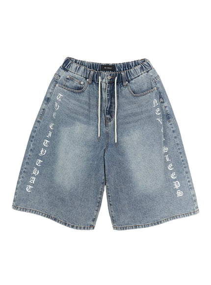Men's 'Never Stop' Graphic Bermuda Jorts (Light Blue) IL507 flat-lay front view, light blue washed denim, old-english vertical graphic prints on both legs, drawstring waist, brand label visible at waistband