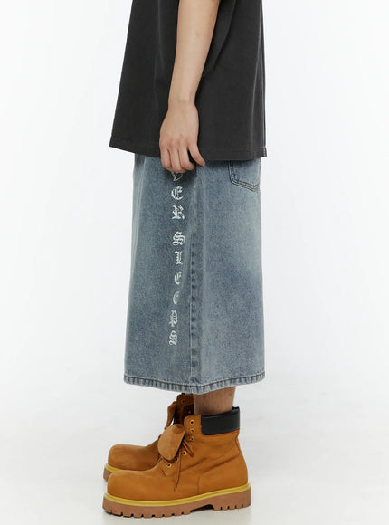 Men's 'Never Stop' Graphic Bermuda Jorts (Light Blue) IL507 right side view on model, wide-leg bermuda length silhouette with vertical old-english graphic print, hand in pocket, styled with tan boots