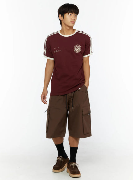 Men's Nylon Cargo Drawstring Bermuda Shorts (Dark Brown) IL507 Dark brown front full-length on male model looking sideways, hand in pocket, wearing burgundy graphic tee and brown shoes