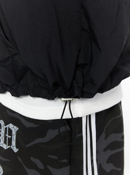 Men's Nylon Hooded Vest IL520 Black close-up detail shot of elastic drawstring hem with metal cord lock toggle and nylon texture