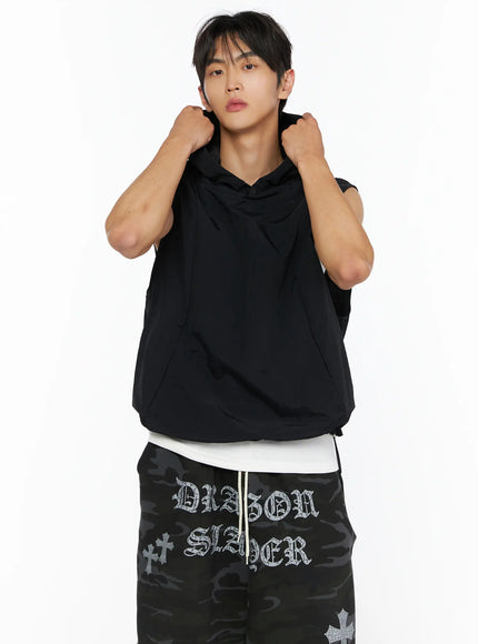 Men's Nylon Hooded Vest IL520 Black close-up front shot on male model gripping hood with both hands, layered over white top
