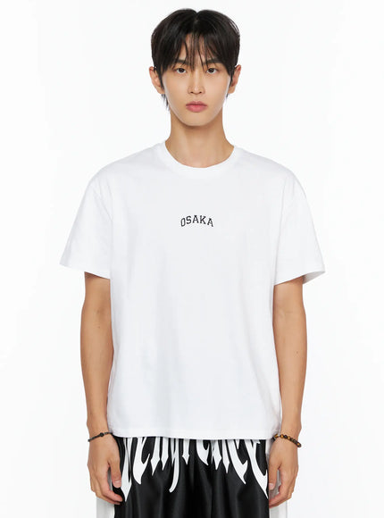 Men's Osaka Graphic T-Shirt IL520 White close-up front shot on model from chest up, showing black OSAKA arch embroidery on white cotton, styled with graphic shorts