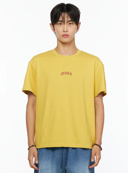 Men's Osaka Graphic T-Shirt IL520 Yellow close-up front shot on model from chest up, highlighting red OSAKA arch embroidery on yellow cotton fabric
