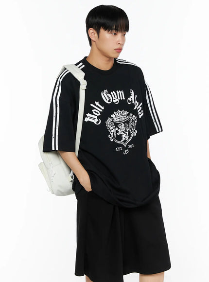 Men's Oversized Athletic Tee IL514 Black side-angle shot on male model carrying white backpack, hand in pocket, white stripe sleeve and gothic crest print detail visible