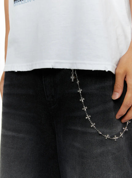 Men's Oversized Graphic T-Shirt IL513 White close-up detail shot of raw distressed hem and silver cross chain accessory against black denim waistband