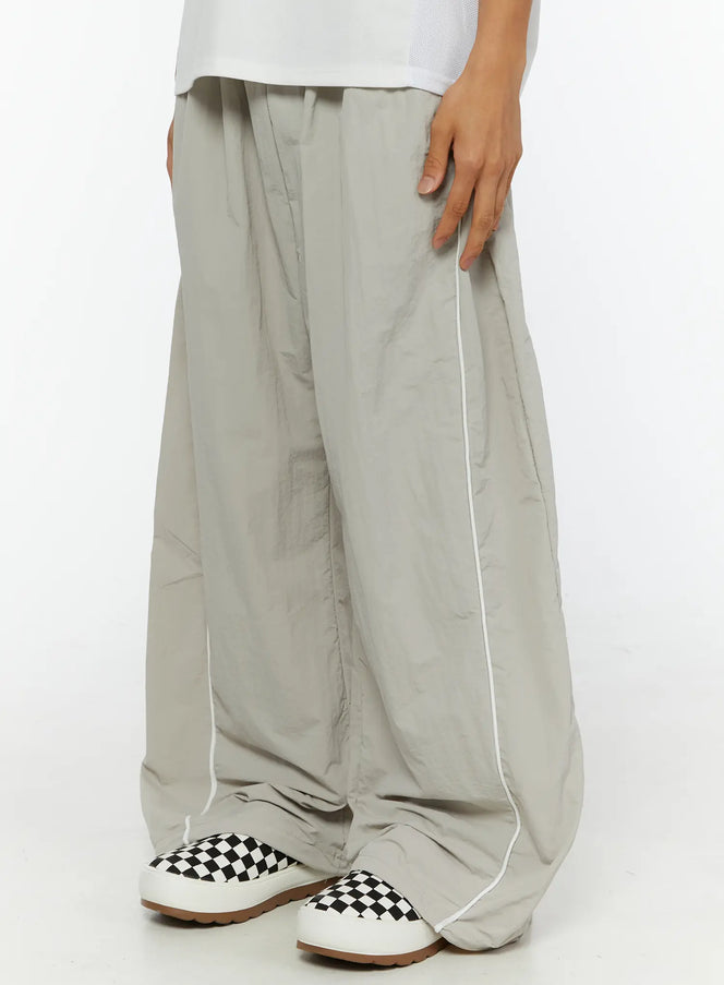Men's Oversized Sweatpants IL510 Light gray side view on model showing white piping seam detail, crinkled nylon wide-leg fit with checkered sneakers