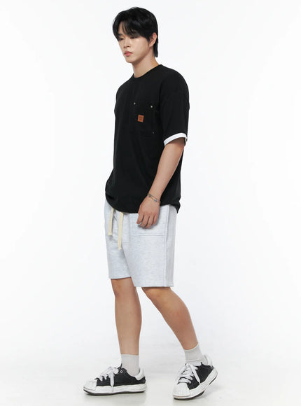 Men's Patch Detail Short Sleeve Tee IU523 Black side view on male model in three-quarter pose, white contrast ringer cuffs, chest pocket with leather patch, paired with light gray shorts