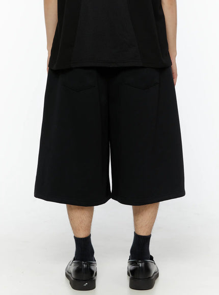 Men's Patch Detail Shorts (Black) IL509 black back view on model, wide-leg silhouette, back welt pocket stitching detail visible, clean plain back panel, loafers styling
