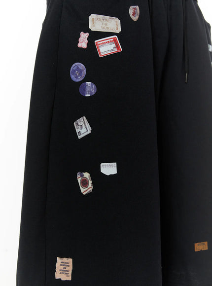Men's Patch Detail Shorts (Black) IL509 black close-up detail, flat angle showing Radiohead ticket, gummy bear, vinyl disc, and currency sticker patches on fabric