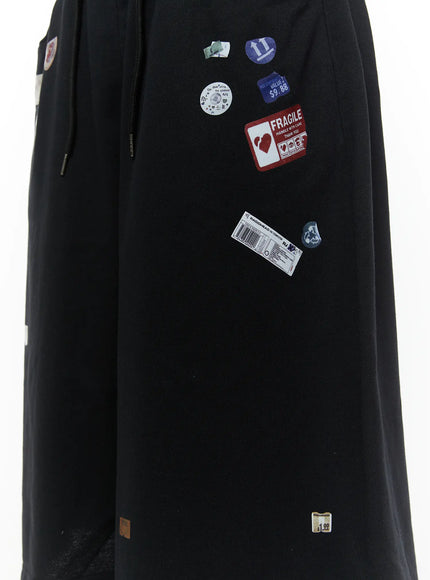 Men's Patch Detail Shorts (Black) IL509 black close-up detail of side panel showing Fragile sticker, $9.88 price tag, barcode, and circular badge patches on black fabric