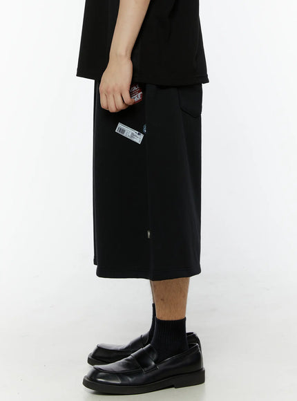 Men's Patch Detail Shorts (Black) IL509 black side view on model, standing straight, showing clean side seam, hem length, and minimal sticker patch detail with loafers