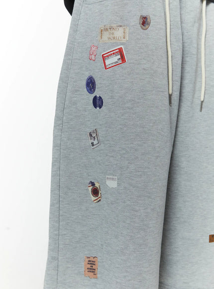 Men's Patch Detail Shorts (Gray) IL509 gray detail close-up of left leg showing Around The World gummy bear Radiohead and circular sticker patches on cotton fabric