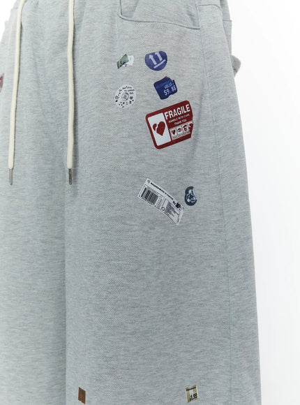 Men's Patch Detail Shorts (Gray) IL509 gray close-up detail shot of front panel showing Fragile handle-with-care barcode and number sticker patches on melange fabric