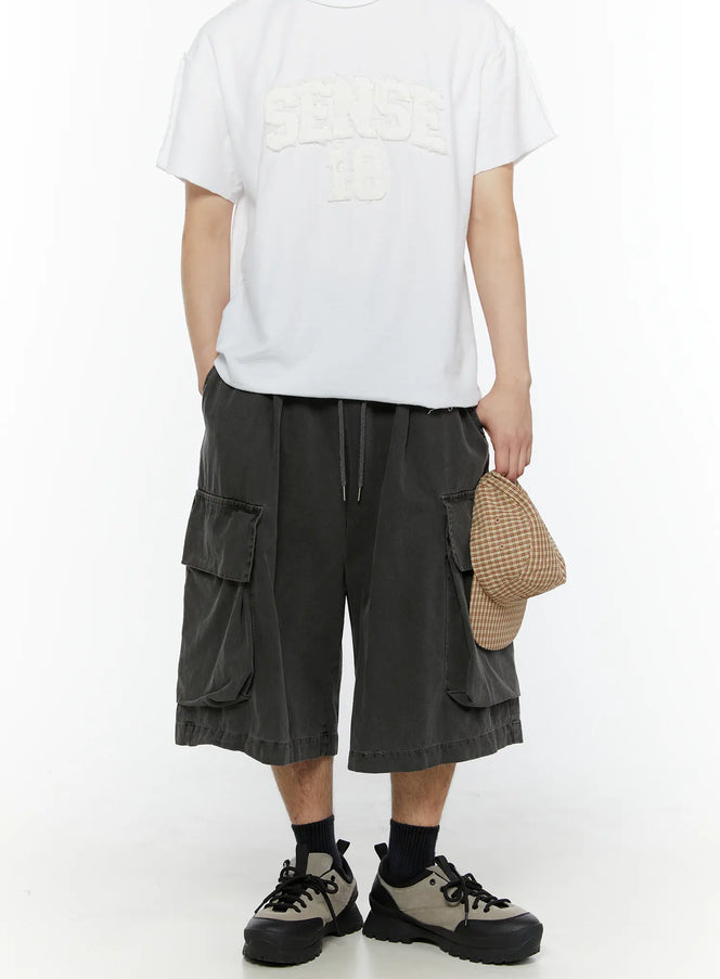LEWKIN Men's Pigment Bermuda Cargo Shorts (Dark Gray) IL507 Dark gray front model shot full-length styled with white graphic tee and sneakers holding plaid cap