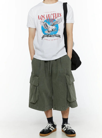 Men's Pigment Bermuda Cargo Shorts (Dark Green) IL507 Dark green full-body front styling shot on male model with Los Angeles graphic tee black shoulder bag and sneakers