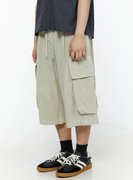 Men's Pigment Bermuda Cargo Shorts (Light Beige) IL507 Light Beige left side shot on male model highlighting oversized single flap cargo pocket and wide-leg silhouette