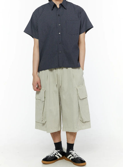 Men's Pigment Bermuda Cargo Shorts (Light Beige) IL507 Light Beige full-body front shot on male model styled with navy grid short-sleeve shirt and black Adidas sneakers