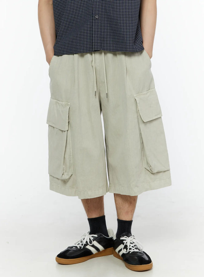 LEWKIN Men's Pigment Bermuda Cargo Shorts (Light Beige) IL507 Light Beige front close-up on male model hands in pockets paired with navy check shirt and sneakers