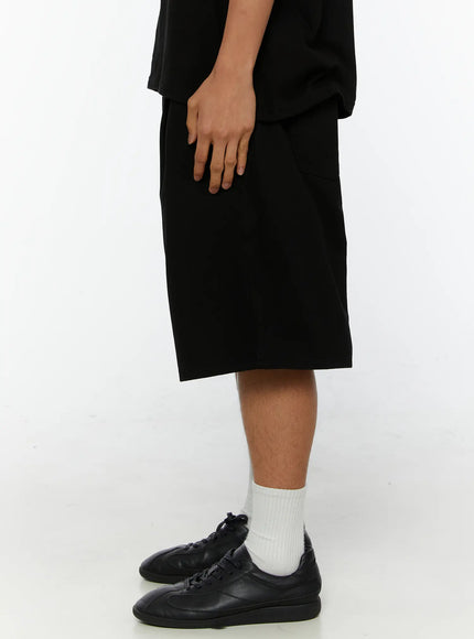 Men's Pintuck Bermuda Shorts IL515 Black side shot on male model showing relaxed wide-leg silhouette length and clean fabric drape with black sneakers