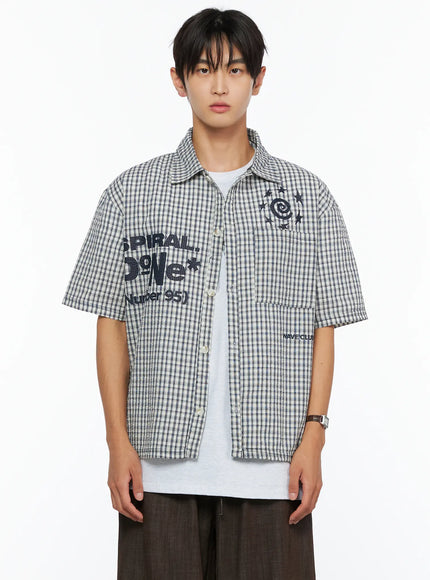 Men's Plaid Graphic Button-Up Shirt IL528 light beige front crop shot on male model open showing SPIRAL DoNe Number 95 embroidery graphic detail on seersucker plaid