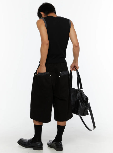 Men's Plaid Pocket Bermuda Shorts (Black) IL507 back view on male model holding black leather bag, showing plaid-paneled back pockets with silver studs