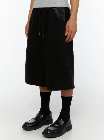 Men's Plaid Pocket Bermuda Shorts (Black) IL507 close-up front view on male model showing drawstring waist, plaid pocket trim and wide-leg hem with loafers
