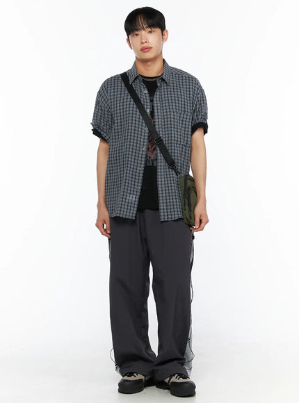 Men's Plaid Roll-Up Short Sleeve Shirt IL514 Gray M/L front full-body shot on model standing facing camera with crossbody bag open over graphic tee and wide cargo pants
