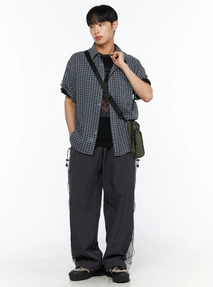 LEWKIN Men's Plaid Roll-Up Short Sleeve Shirt IL514 Gray M/L full-body styled shot on model posed at angle with crossbody bag layered over graphic tee and wide-leg pants