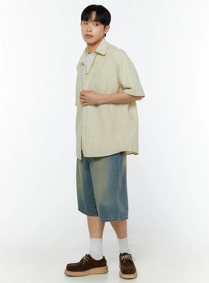 Men's Plaid Short Sleeve Shirt IU529 Light yellow three-quarter side shot on male model holding shirt hem showing relaxed oversized fit layered over white tee