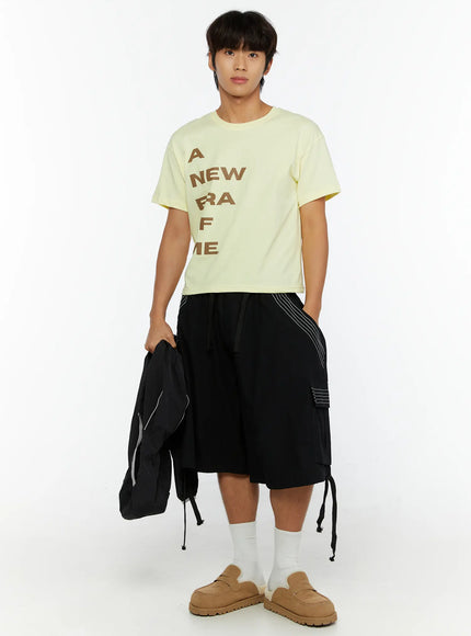 Men's Pocket Cargo Shorts IL515 Black front full-body shot on male model holding black jacket with white contrast stitch accents