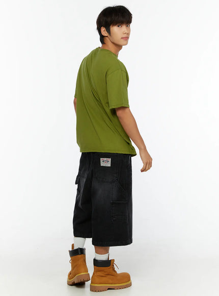 Men's Relaxed Denim Carpenter Shorts IL513 Black three-quarter back view on male model, brand patch on back pocket visible, styled with olive tee and tan boots