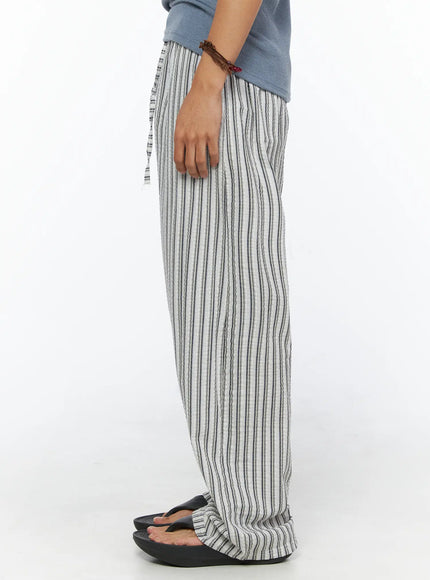 Men's Relaxed-Fit Pajama Pants IL520 Dark blue side shot on model showing relaxed wide-leg silhouette seersucker stripe texture and gathered hem pooling over sandals