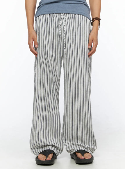 LEWKIN Men's Relaxed-Fit Pajama Pants IL520 Dark blue front close-up on model wearing wide-leg seersucker stripe trousers with button fly and elastic waist styled with sandals