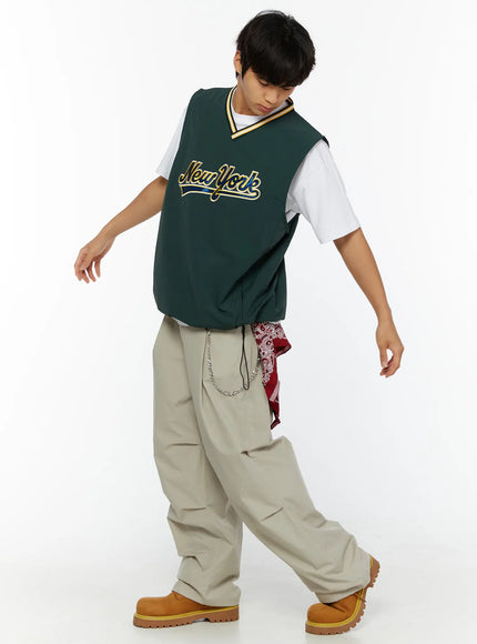 Men's Relaxed-Fit Parachute Pants IL509 Light beige full-body dynamic shot on model in green baseball vest mid-stride showing wide draping parachute legs