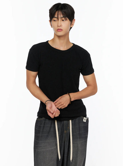 Men's Ribbed Slim-Fit T-Shirt IL520 Black cropped front shot on male model with hands clasped wearing ribbed knit texture styled with dark wide-leg pants