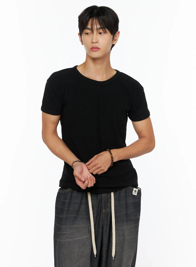 Men's Ribbed Slim-Fit T-Shirt IL520 Black cropped front shot on male model with hands clasped wearing ribbed knit texture styled with dark wide-leg pants