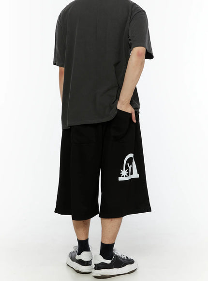 Men's Shooting Star Printed Shorts (Black) IL509 back view on male model showing wide-leg cut and white arch figure graphic print on lower hem, paired with grey tee