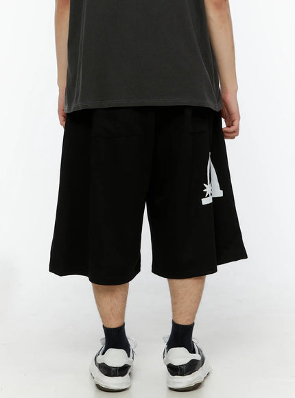 Men's Shooting Star Printed Shorts (Black) IL509 back close-up on male model showing white arch figure graphic on lower right leg, wide flared hem detail