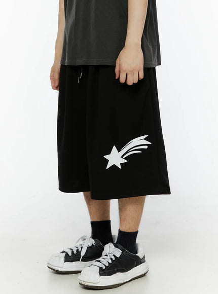 Men's Shooting Star Printed Shorts (Black) IL509 front close-up on male model highlighting white shooting star graphic and drawstring elastic waistband, wide-leg fit