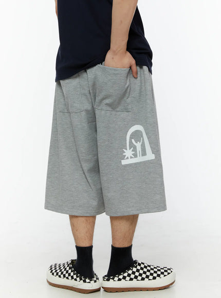 Men's Shooting Star Printed Shorts (Gray) IL509 Gray back side view on model showing hand in pocket, white arch figure graphic on left leg, wide-leg cut in heathered cotton fleece