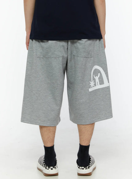 Men's Shooting Star Printed Shorts (Gray) IL509 Gray back view on model showing two back patch pockets, elastic waistband, and white arch figure logo print on right leg