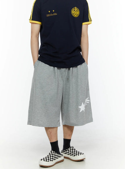 Men's Shooting Star Printed Shorts (Gray) IL509 Gray front view on model styled with navy football club tee, hands in pockets, wide oversized leg with white shooting star print visible